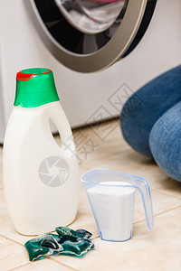 洗粉涤剂和在浴室的机器旁边测量杯子家务衣物洗涤器概念衣粉涤剂图片