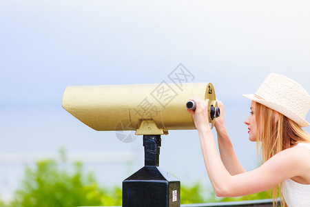 穿戴太阳帽子的女游客透过望远镜向处看图片