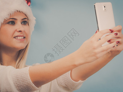 现代假日概念穿着圣诞礼帽的金发女人给自己拍圣诞照用智能手机自拍图片