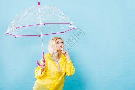 身穿黄色雨衣的金发妇女拿着透明的雨伞检查天气是否在下雨时表现出静默的姿态图片