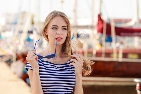 时装金发女孩蓝心的太阳眼镜在码头对港口的游艇图片