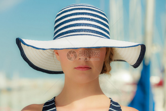 夏天时装概念的有吸引力女孩身戴大条纹帽子在码头与港口游艇对着码头的关闭图片