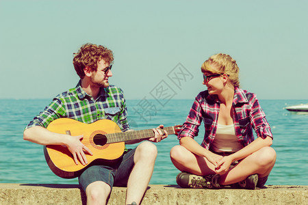 年轻男人在外户和女友弹吉他夏日阳光明媚的夏日海边情侣约会浪漫图片