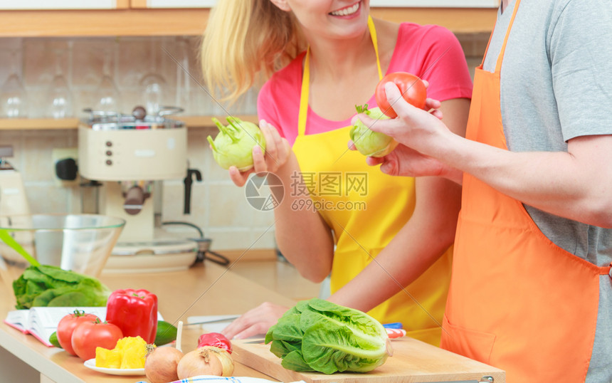 快乐的年轻夫妇做饭女人和男在家里的现代厨房做新鲜蔬菜食品沙拉时玩得开心图片