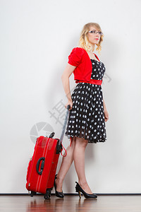 旅行度假概念身穿波尔卡圆点黑色高跟鞋准备出行的红色手提箱全身穿着波尔卡圆点黑衣服的优美年轻女子背景图片