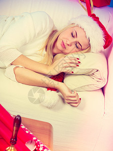 睡在穿着圣塔帽的沙发金女人身上等待礼物室内拍摄睡在圣塔帽上的金发女人图片