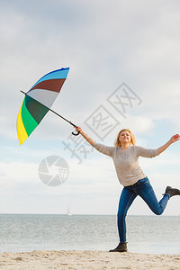 幸福享受天气感美好理念女人在海边滩上阳光明媚的白天和清蓝空上带着多彩的雨伞跳女人在海滩上带着多彩的雨伞跳跃图片