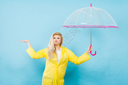身穿黄色雨衣的金发女人拿着透明的雨伞检查天气是否下雨图片