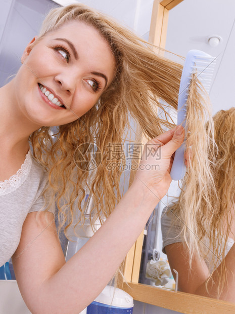 女人在浴室洗澡后梳她的长卷发看着镜子金发女孩早上在洗时注意刷新型理概念女人在浴室梳长发图片