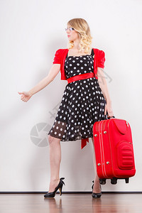 穿着Polka圆点黑裙子的美丽可爱女人准备搭便车旅行的红色手提箱举高穿着红色手提箱搭便车的女人图片