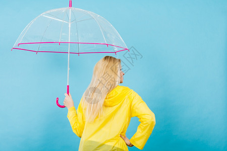 穿着雨衣的金发妇女持透明伞背视图片