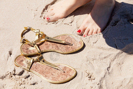 女人的脚和红色钉子紧靠着优雅的翻滚在沙滩上鞋夏季时间图片