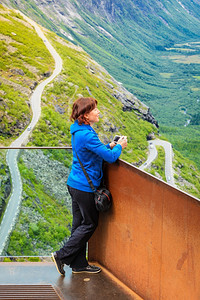旅行概念观光女游客看TrollsTrollstigen或Trollstigveien绕风景山路用照相机从挪威欧洲的观景点拍摄图片