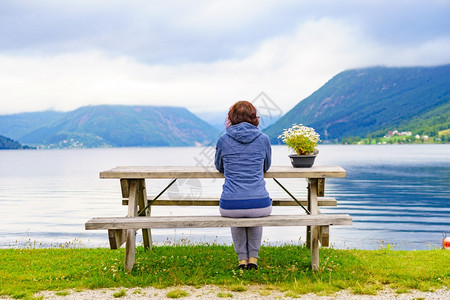旅游概念坐在海边长椅上坐在海边的成熟旅游女观望着挪威的fjords风景图片