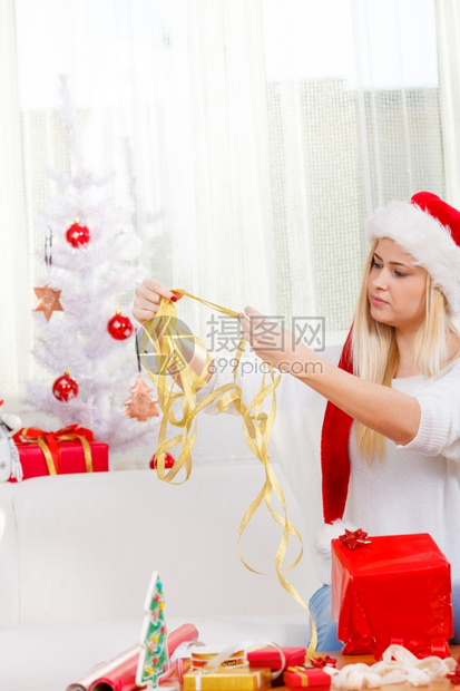 节日礼物季节概念戴圣诞帽的女人坐在沙发上准备和打包圣诞礼物戴圣诞