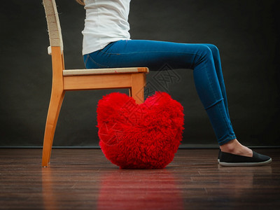 心碎的爱情概念坐在椅子上的地板深暗背景的红心枕头上女人图片
