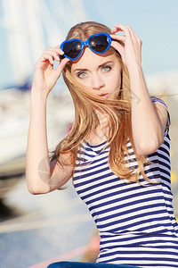 夏天和人的概念时装可爱的金发美女心型太阳眼镜在码头与港口的游艇对着码头图片