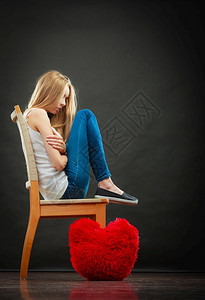 心碎的爱情概念坐在椅子上地板深底黑暗背景的红心枕头上悲哀不幸妇女图片