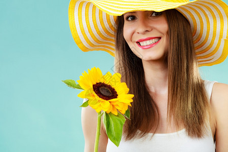 穿着黄帽子的有吸引力夏日女子肖像蓝色背景的向日葵手握着图片