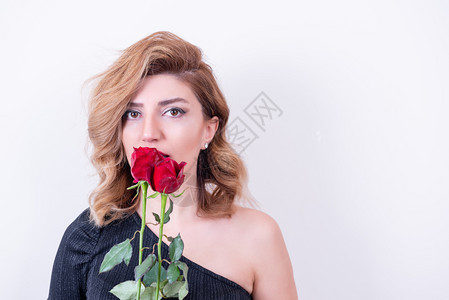 迷人的美女模特闻到两朵红玫瑰的香味与白色背景隔绝图片