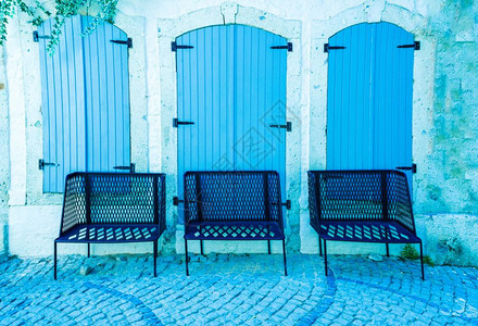 白色混凝土石墙背景有3个蓝色的闭木窗和3个金属椅子前侧图片