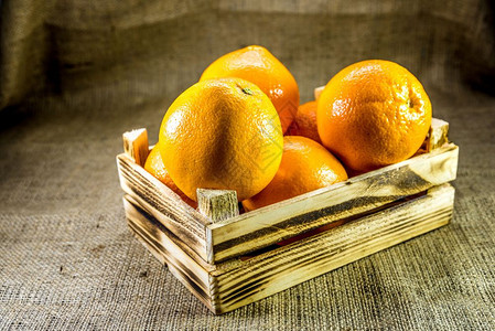 在旧的烧熟木制箱或有麻布背景的盒子中鲜熟橙水果图片