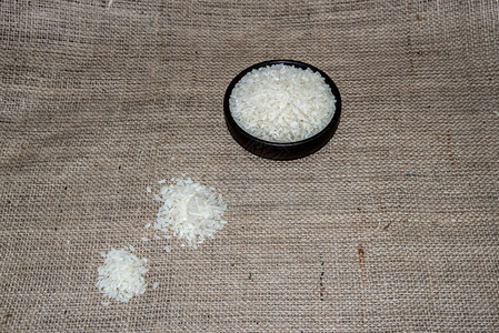 在乡村布袋的背景上满是米饭的木头弓米饭在深色的木碗里复制空间供编辑麻布背景木蝴蝶结米图片