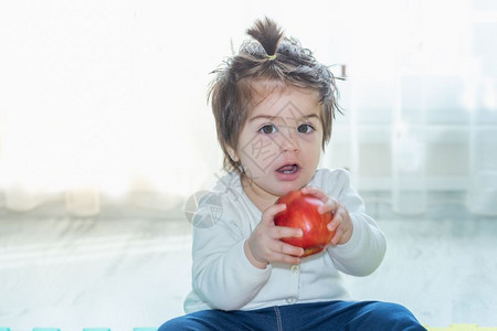 可爱小女婴的肖像她抱着吃一个大红苹果图片