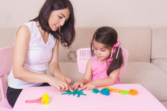 母亲和可爱的女孩坐在桌子上玩橡皮泥图片