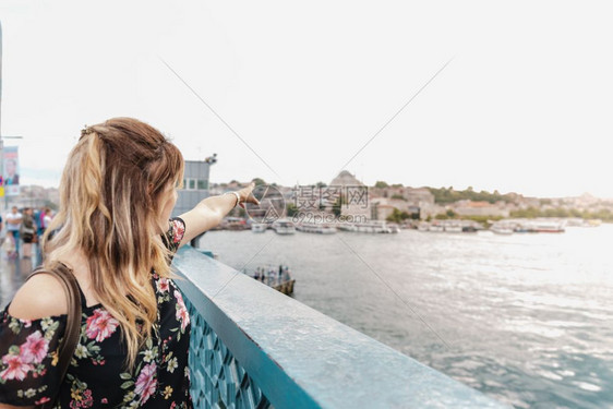 美丽的女在土耳其伊斯坦布尔的加拉塔桥上展示Suleymaniye清真寺和埃米诺努镇图片