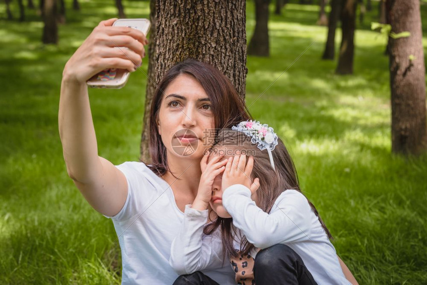 年轻妈和小女孩一起拍自小女孩把脸藏起来年轻母亲和女儿的相在绿草上拍自图片