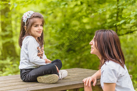 年轻妈和她的小女孩一起在森林中的木板凳上玩得很开心图片