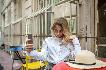 有吸引力的年轻美女坐在外面的咖啡厅里时使用智能电话图片