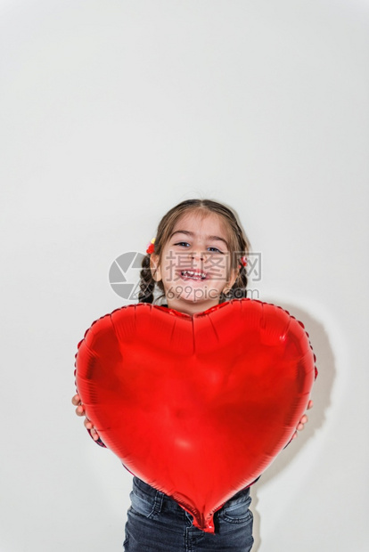 可爱的小女孩拿着红心气球与孤立背景的假日概念穿着校服的可爱快乐女孩肖像图片