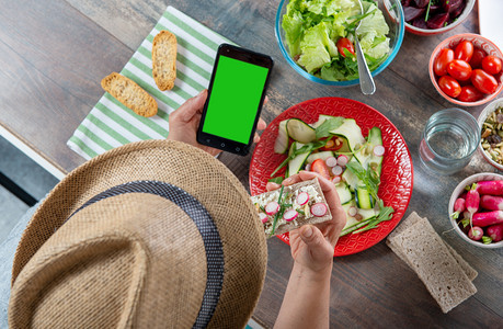 一个女人吃素食沙拉使用智能手机绿色屏幕顶级视野图片