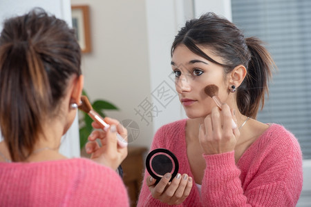 一个年轻的黑发女人在镜子里化妆图片