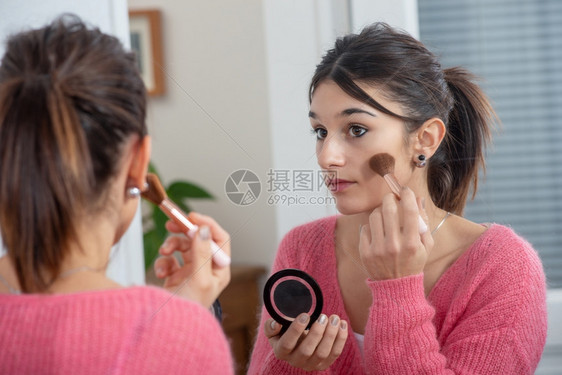 一个年轻的黑发女人在镜子里化妆图片