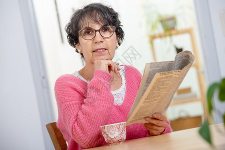 穿着粉色红衣服的美丽黑发成年妇女阅读报纸图片