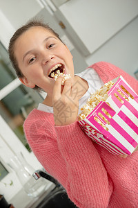 带着粉红色毛衣在家里吃爆米花的年轻少女图片