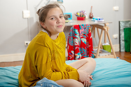 一个年轻的少女坐在床上交叉腿图片