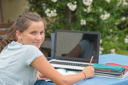 十几岁的女孩在花园里用笔记本电脑做家庭作业图片