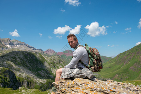 一个年轻男子徒步旅行者坐在山中的岩石上图片