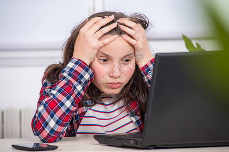 一个无聊的少女正在用笔记本电脑做家庭作业图片