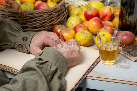 一个男人用苹果酒杯在旧笔记本上写作图片