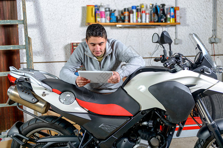 一个年轻人使用摩托车旁边的平板电脑图片