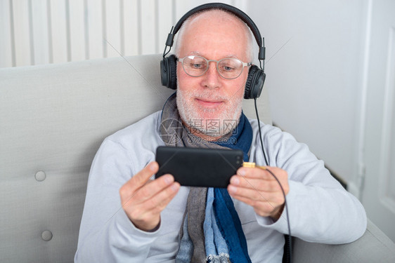 快乐的老人用耳机在家里听音乐图片