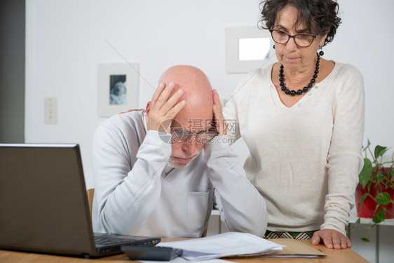 一个成熟夫妇在家里用笔记本电脑支付账单图片