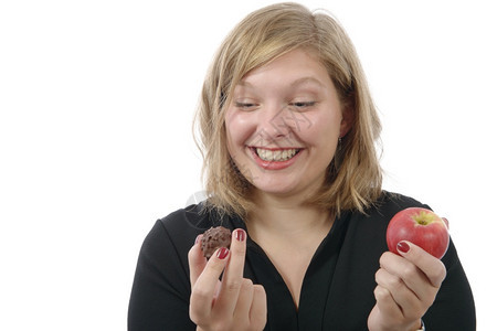笑着的年轻女子在巧克力和苹果之间犹豫不决图片