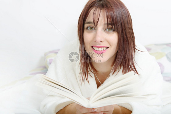 美丽的笑女孩在床上看书图片