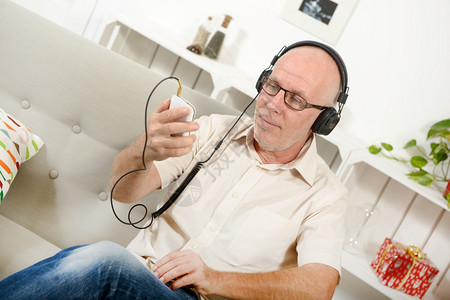 英俊的成熟男子在家里用耳机听音乐图片